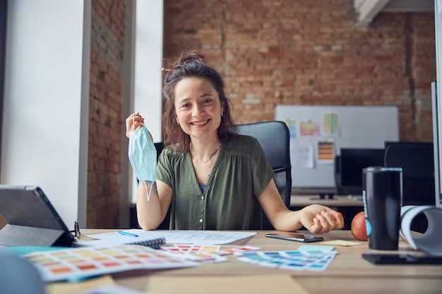 Donna sorridente interior designer che tiene maschera protettiva e guarda la telecamera che lavora con il colore