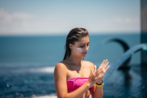 Smiling woman is applying sunscreen on her face