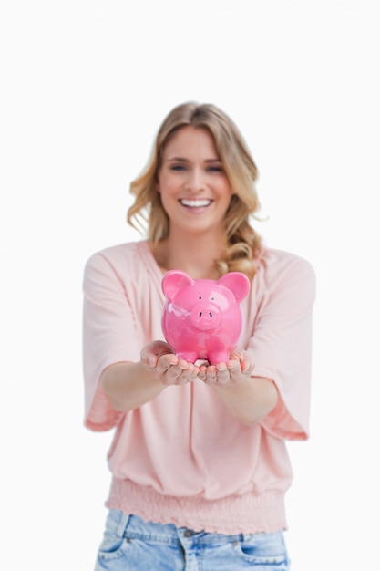 A smiling woman is holding a piggy bank in the palms of her hands