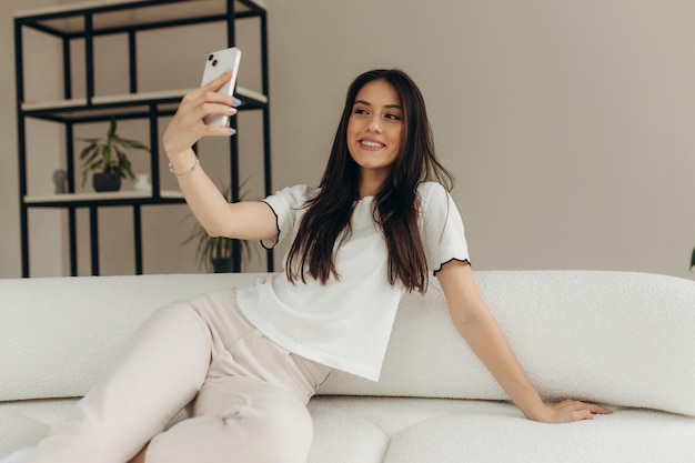 Smiling woman is taking a selfie on the sofa at home