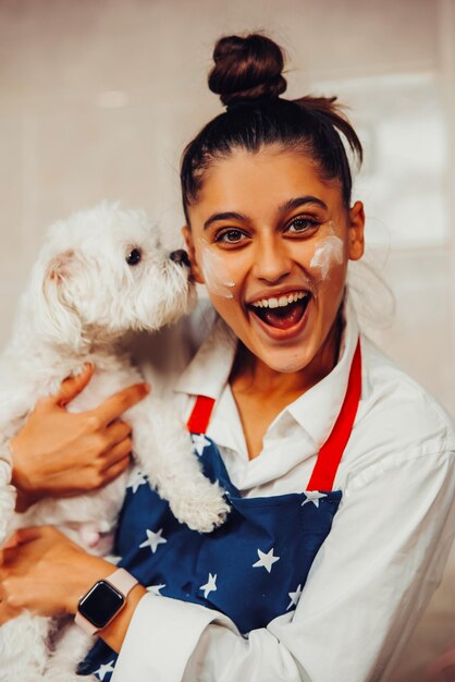 Foto donna sorridente in cucina che tiene un simpatico cane maltese bianco