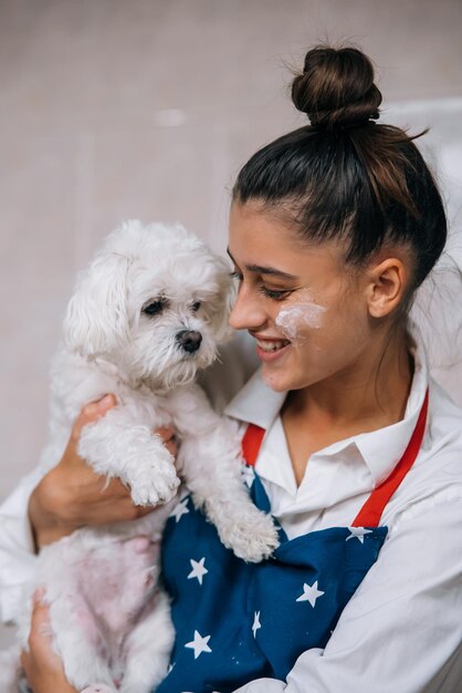 かわいい白いマルチーズ犬を保持しているキッチンで笑顔の女性