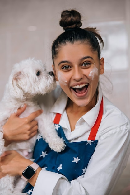 かわいい白いマルチーズ犬を保持しているキッチンで笑顔の女性