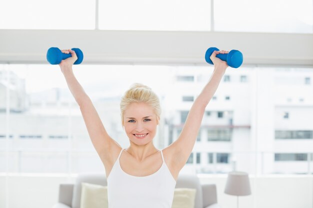 Smiling woman lifting dumbbells at fitness studio