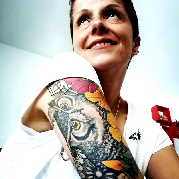 Улыбающаяся женщина отворачивается, показывая татуировку.