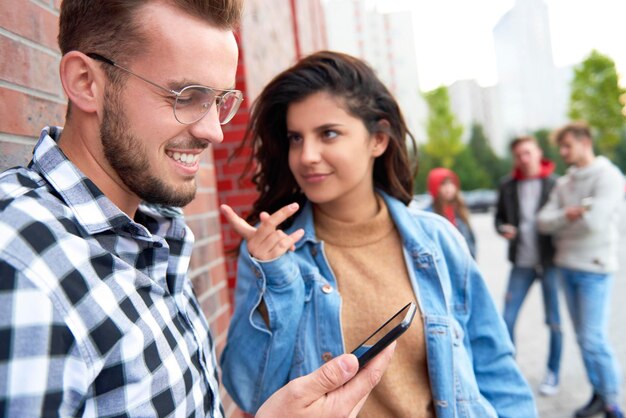 Photo smiling woman looking at friend using mobile phone against wall