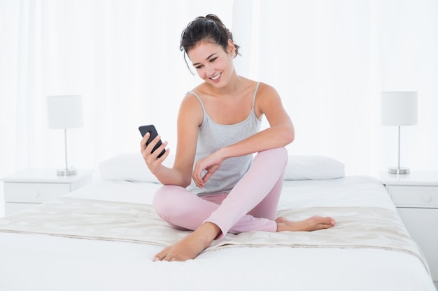 Smiling woman looking at mobile phone in bed