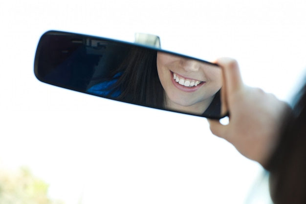 Photo smiling woman  looking in the rear-view mirror