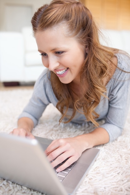 Donna sorridente che si trova sul tappeto con il suo laptop