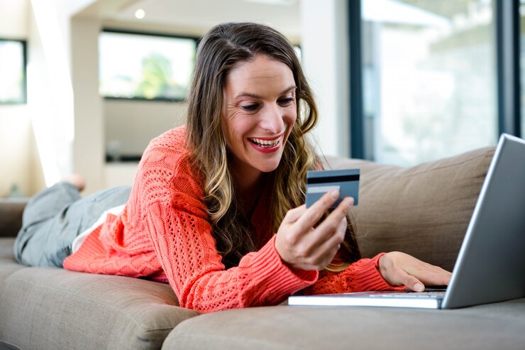 Photo smiling woman lying on the couch with her laptop and credit card