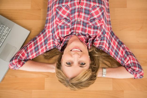 Foto donna sorridente che si trova sul pavimento accanto al computer portatile