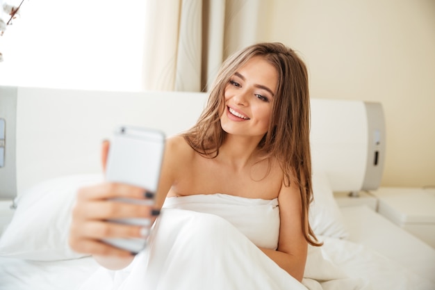 Photo smiling woman making selfie photo on the bed at home