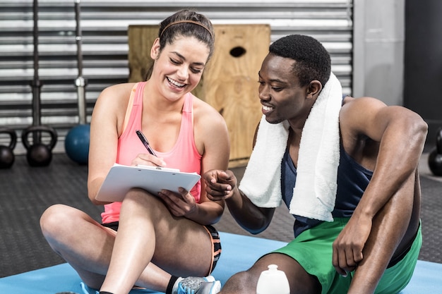 Smiling woman and man writing on paper at gym