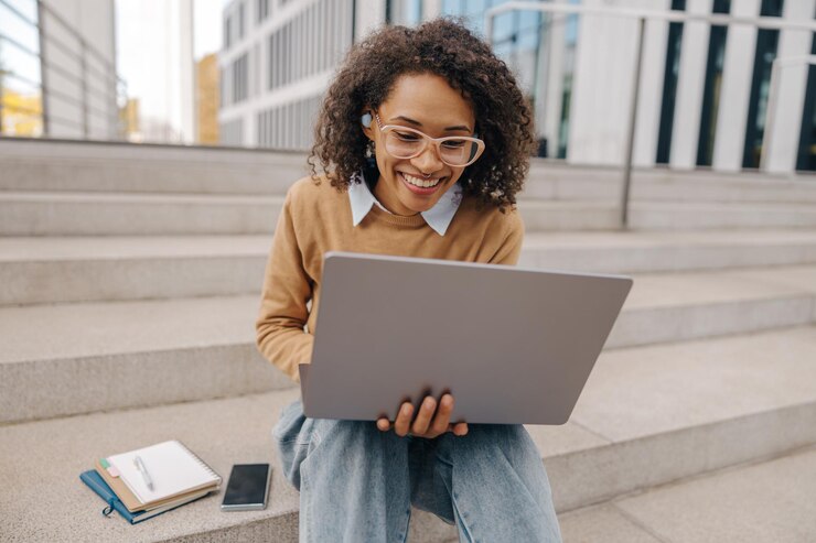 Photo smiling woman manager in eyeglasses is working on laptop sitting on background of office building