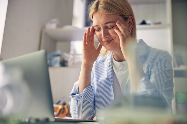 Smiling woman massaging her temples with closed eyes while keeping elbows on table