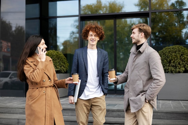 Smiling woman and men communicate on street near modern glass building Girl talking on mobile phone