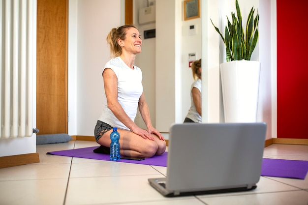 La donna sorridente nel salone moderno guarda le esercitazioni di forma fisica su internet tramite computer portatile.