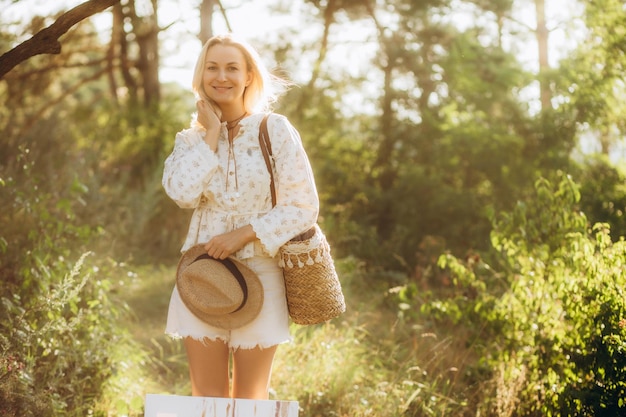 smiling woman in nature with wicker bag and hat