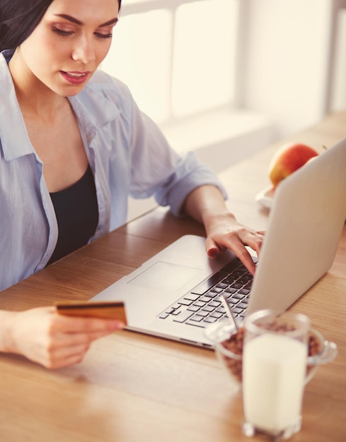 Smiling woman online shopping using computer and credit card in kitchen