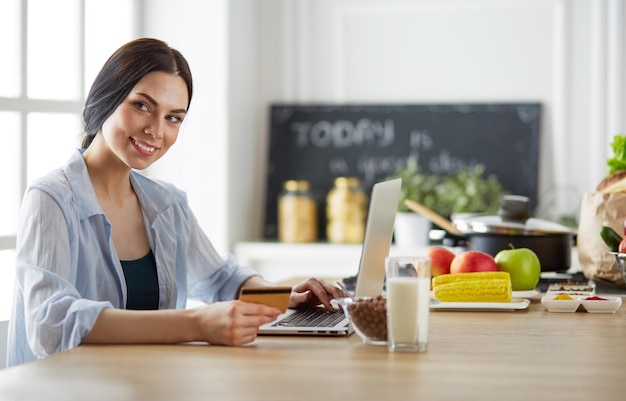 Smiling woman online shopping using tablet and credit card in kitchen