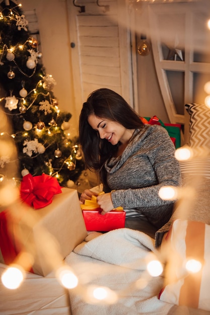 Smiling woman opening gift box sitting at home during christmas