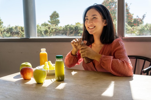 Smiling woman opening a healthy fruit smoothie sitting and receiving the sunlight