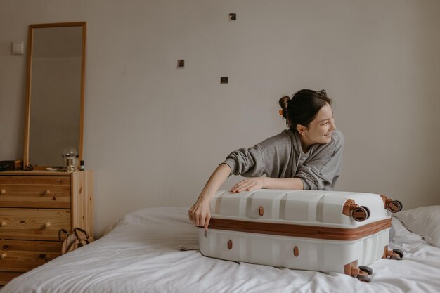 Photo smiling woman packing her suitcase at home on the white bed