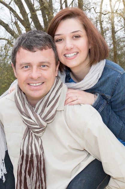 Smiling woman piggyback on her man while looking at camera outdoors