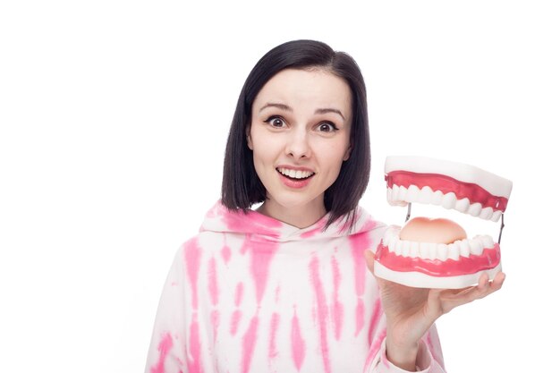 smiling woman in a pink hoodie holds a dental jaw in her hand white background