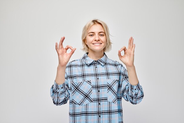 Smiling woman in plaid shirt making OK sign with hand on a light background