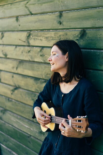 Photo smiling woman playing guitar while standing by wall outdoors