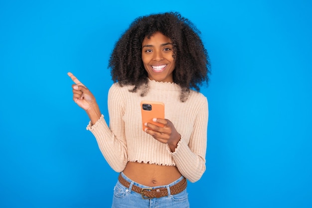 Smiling woman pointing finger at blank space holding phone in one hand Copy space