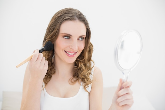 Smiling woman putting powder on her cheeks 