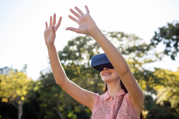 Smiling woman raising her hands while using a VR headset in the park