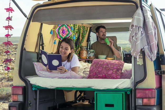 Photo smiling woman reading book against man having breakfast in motorhome