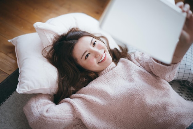 家でベッドで本を読んでいる笑顔の女性