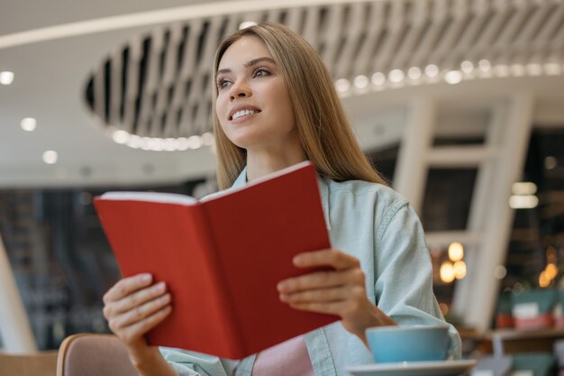 Smiling woman reading book, sitting in cafe