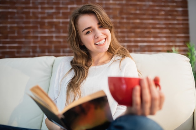 リビングルームで飲みながら本を読んで笑顔の女性