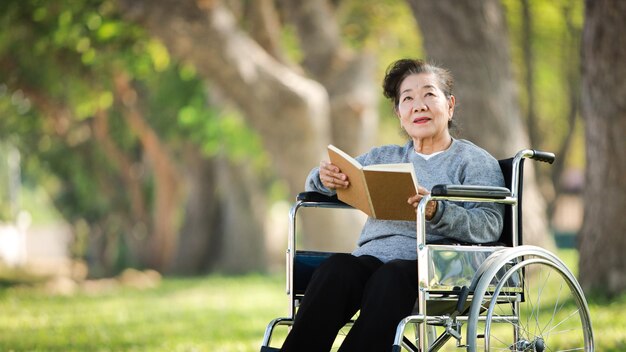 Photo smiling woman reading while sitting on wheelchair over grassy land