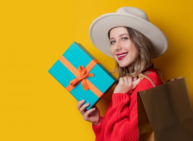 Smiling woman in red sweater with gift box and shopping bag 