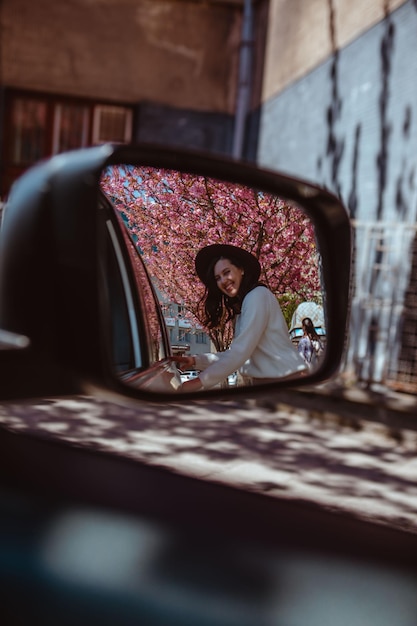 배경에 꽃이 만발한 자동차 후면 거울에 웃는 여자 반사
