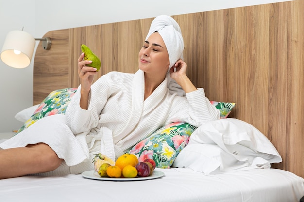 Foto donna sorridente che si rilassa a letto mangiando pere