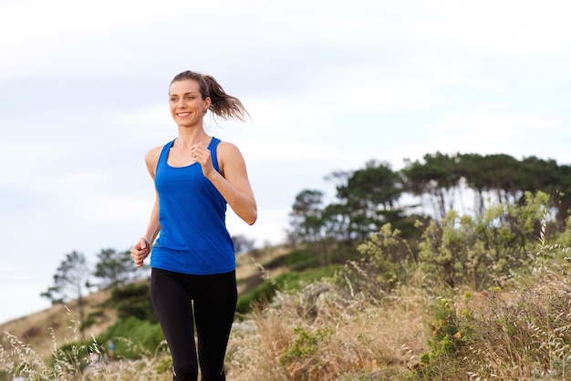 Donna sorridente che corre fuori in abiti sportivi