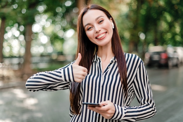 Photo smiling woman in shirt shows thumbs up on the street