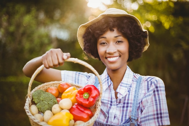 Smiling woman showing a basket of vegetables in the garden