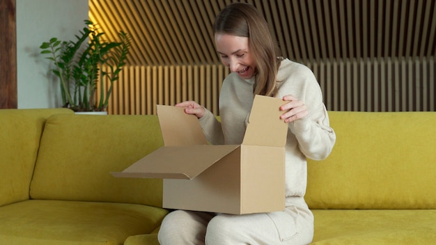 Smiling woman sit on sofa at home open cardboard delivery package shopping online