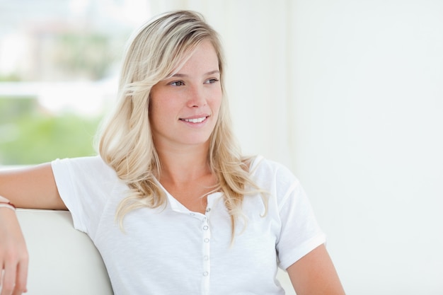 A smiling woman sits on the couch as she looks over to the side 