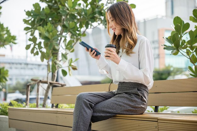 スマートフォンを使ってソーシャルメディアでチャットする屋外の公園のベンチに座っている笑顔の女性