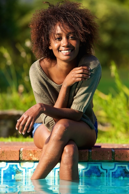 smiling woman sitting by pool with feet in water