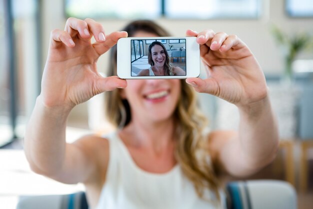 彼女の携帯電話でselfieを取ってソファに座って笑顔の女性